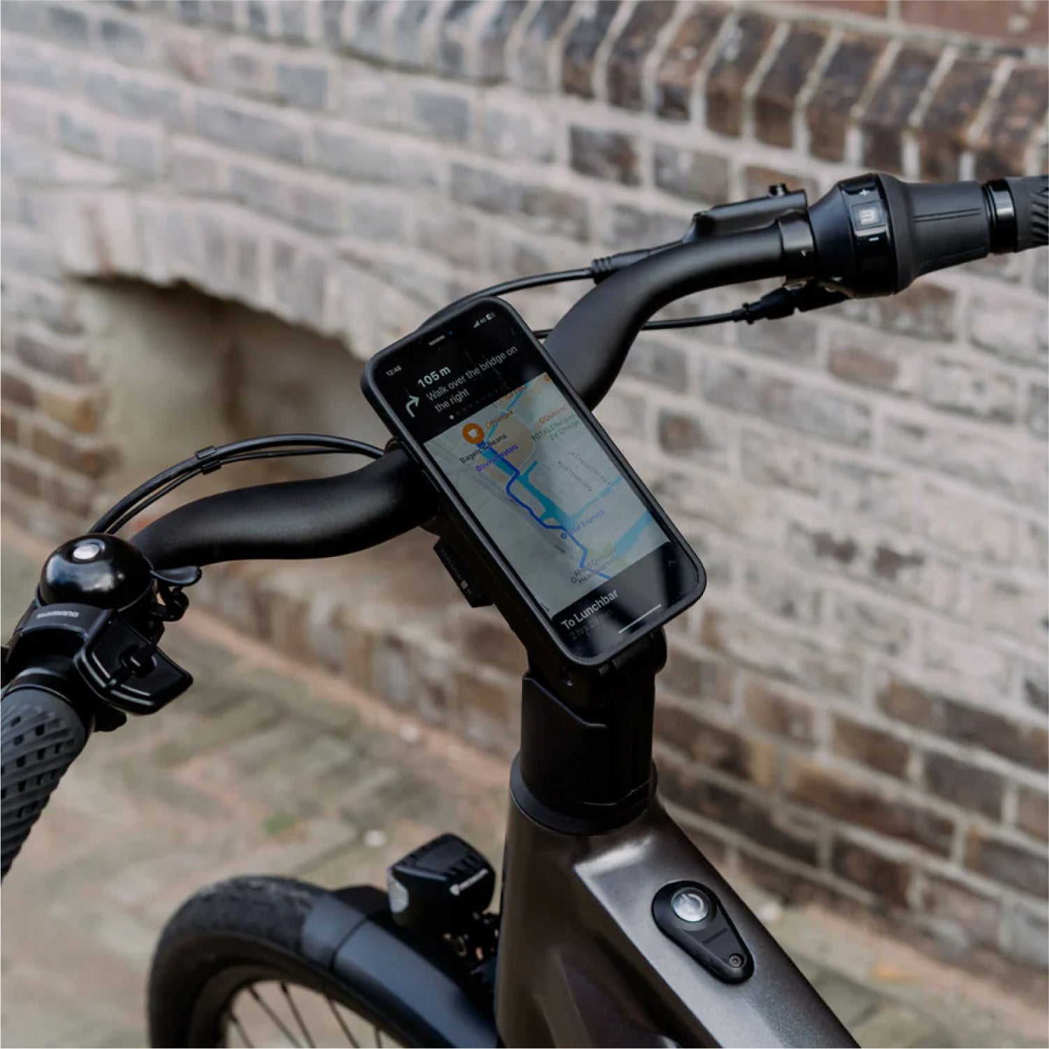 Detailshot van smartphone met Google Maps navigatie app + onderdelen Shimano versnellingen, Shimano display en bel op stuur Levante E4 e-bike