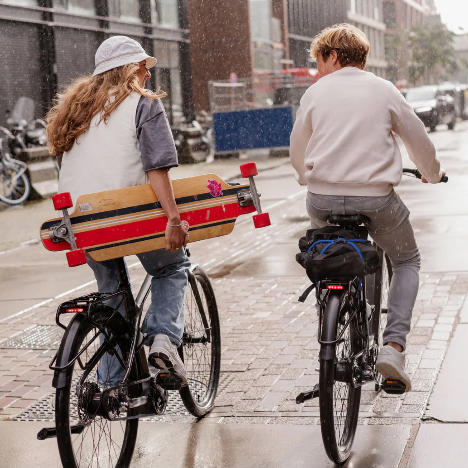 Tiener jongen en tiener meisje op donkergrijze Levante E4 e-bikes fietsend door de regen met skateboard en rugtas