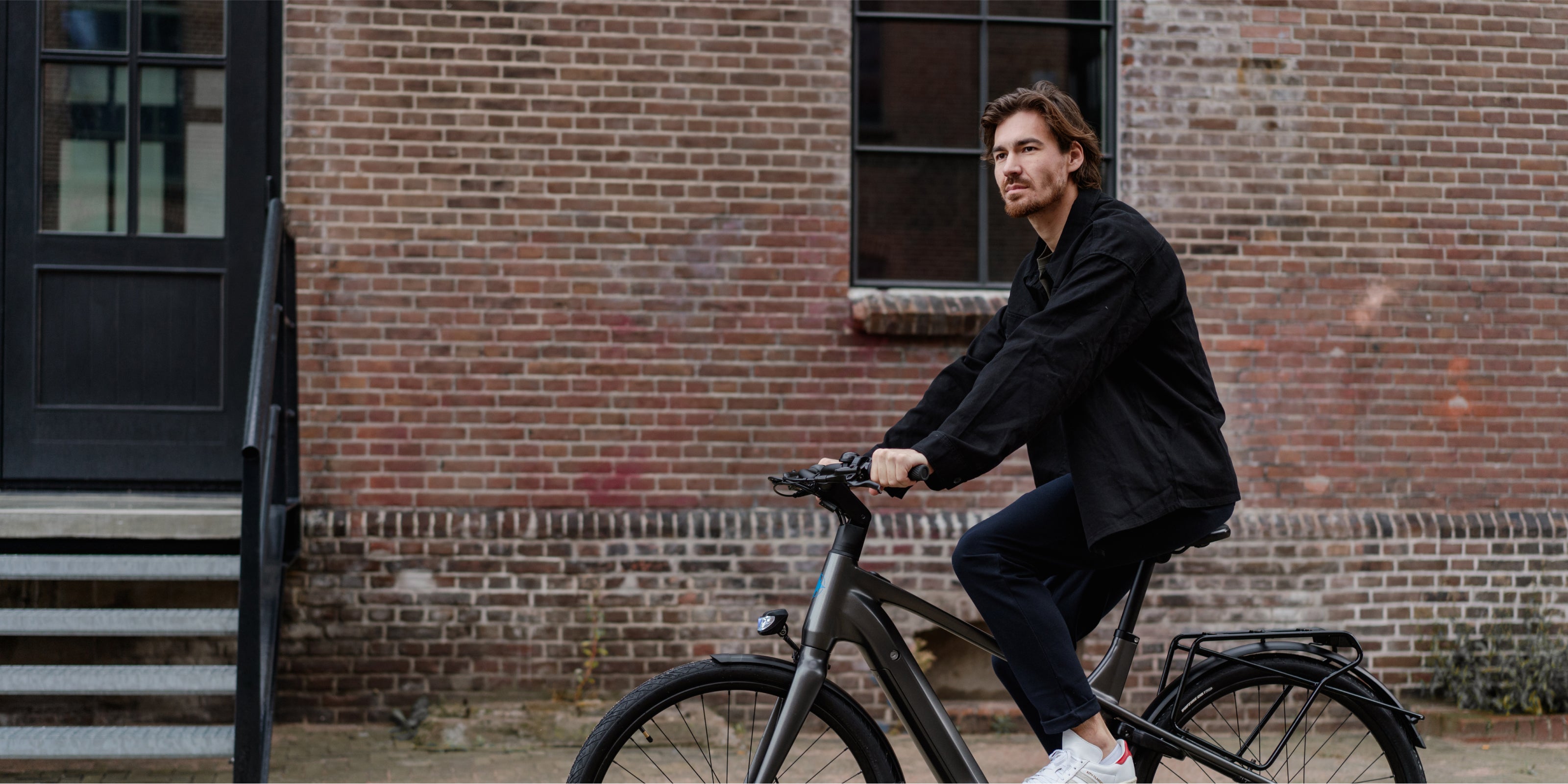 Man met donker haar fietsend op donkergrijze Levante E4 e-bike voor stenen muur